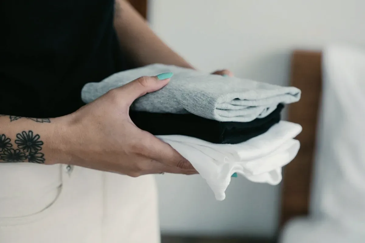 Hands holding a stack of folded clothes.