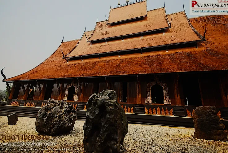 A dark wooden hall of Baan Dam, the Black House, with black stones in front.