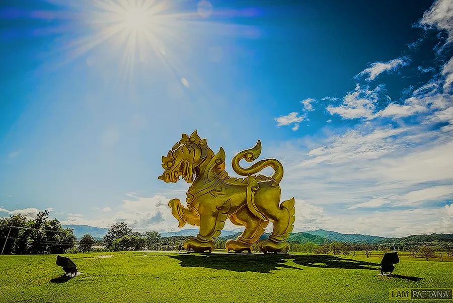 The golden lion of Singha Park on a green lawn, the hills behind.