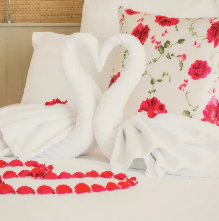 Two towel swans on a bed with red petals.