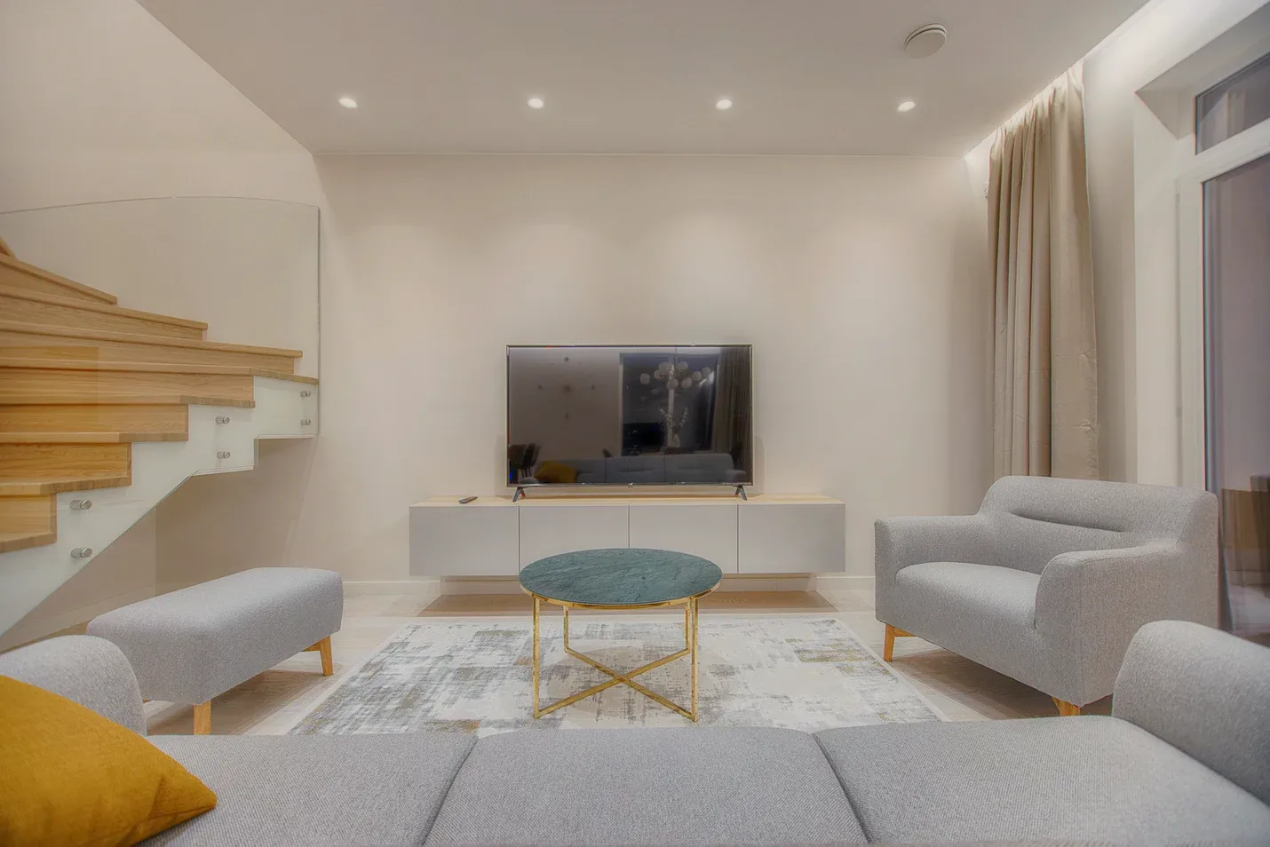 A living room with a grey sofa, a round brass table and a staircase.