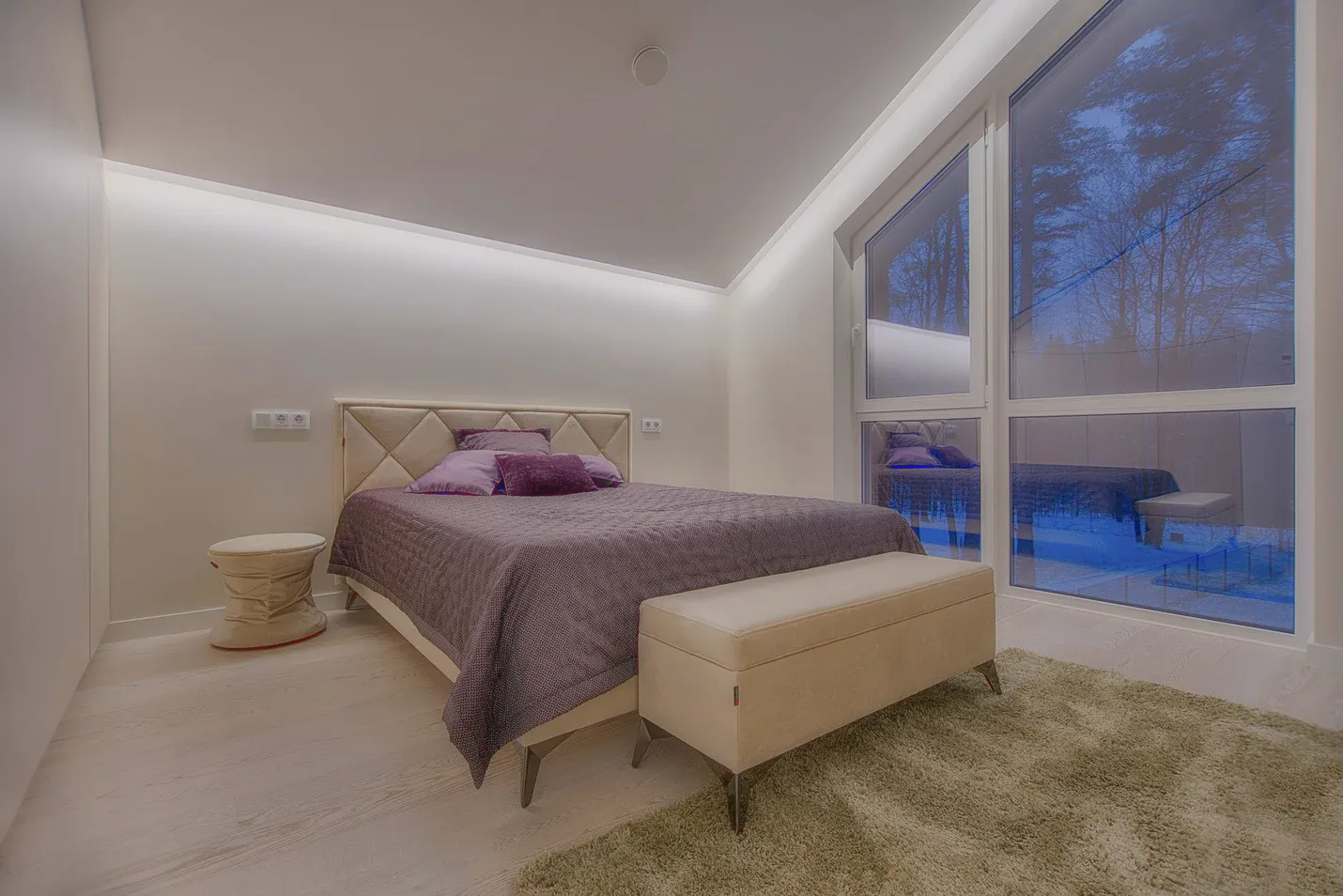 A bedroom with a tall window, a purple bedspread and a deep rug.