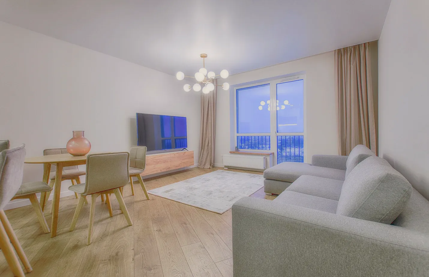 A living room with grey sofas, a dining table and a chandelier.